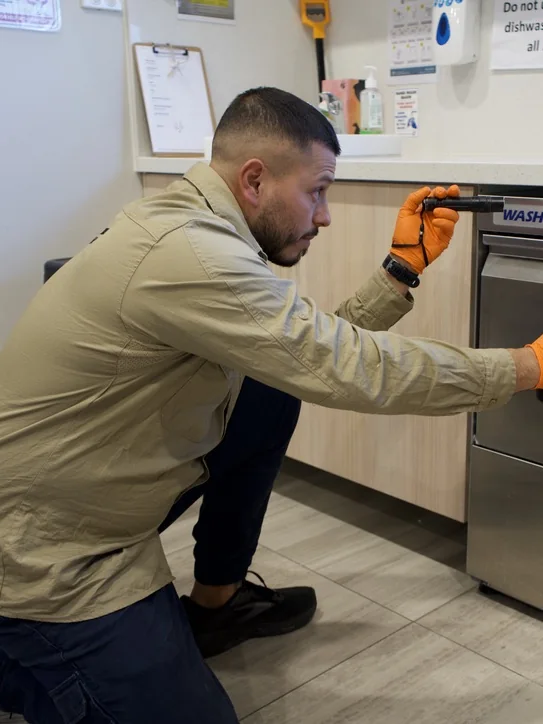 Jimmy inspecting around a commercial dishwasher for Extreme Pest Control NSW
